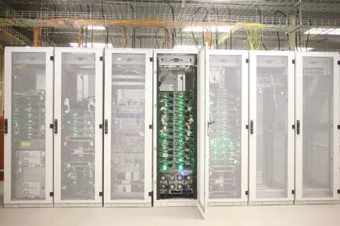 Server cabinets in a data-center hall, one door open on populated racks and overhead cable trays.