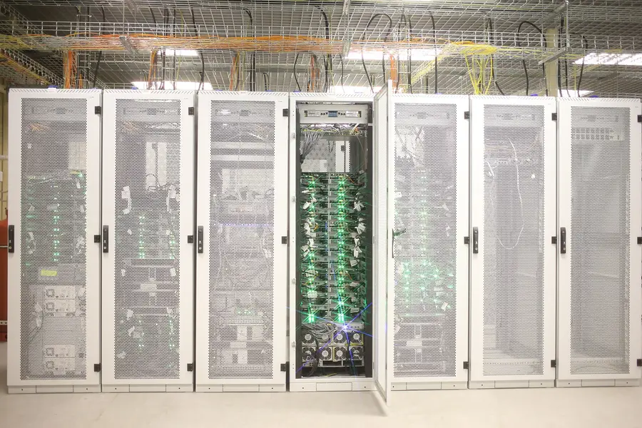 Server cabinets in a data-center hall, one door open on populated racks and overhead cable trays.