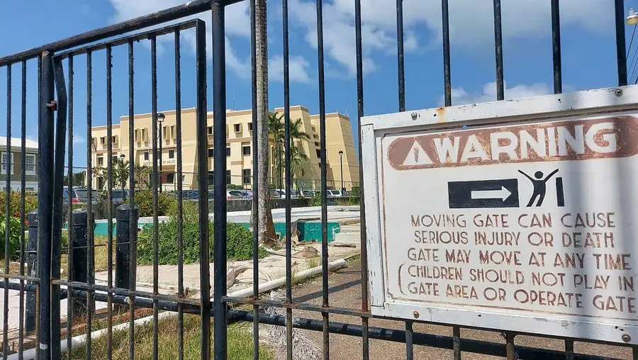 Central Bank of Belize building seen through a black metal gate, with a warning sign about a moving gate in the foreground