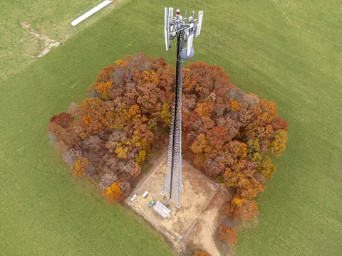 Aerial photograph of a lattice cell tower with panel antennas inside a fenced compound