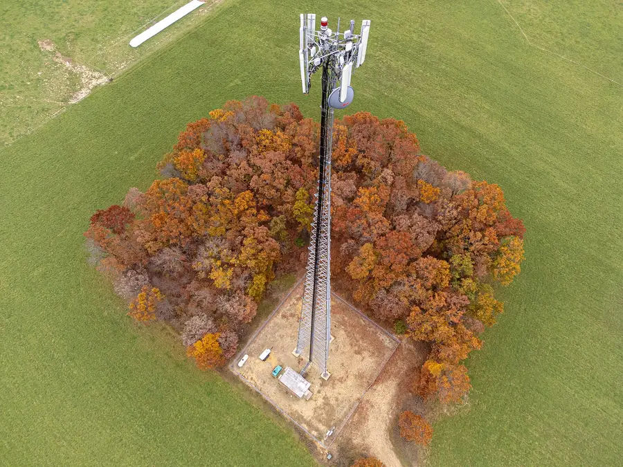 Aerial photograph of a lattice cell tower with panel antennas inside a fenced compound