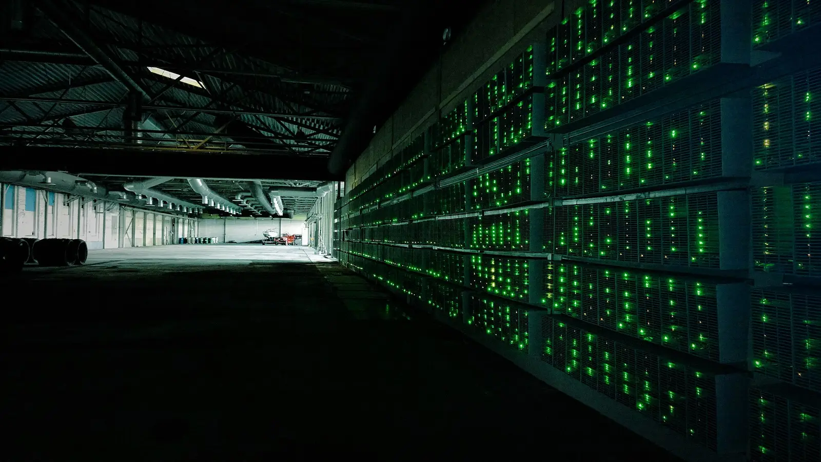Racks of cryptocurrency mining hardware lit by green status LEDs inside a large proof-of-work mining facility
