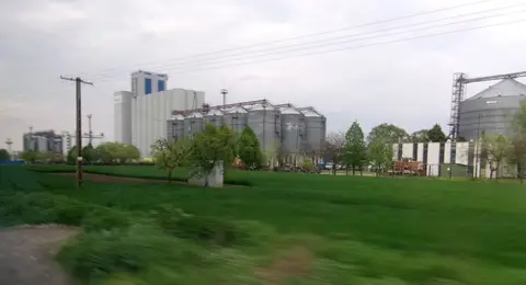 The Bunge oilseed processing plant at Martfű, Hungary, with grain silos and a green field in front, photographed in April 2026.