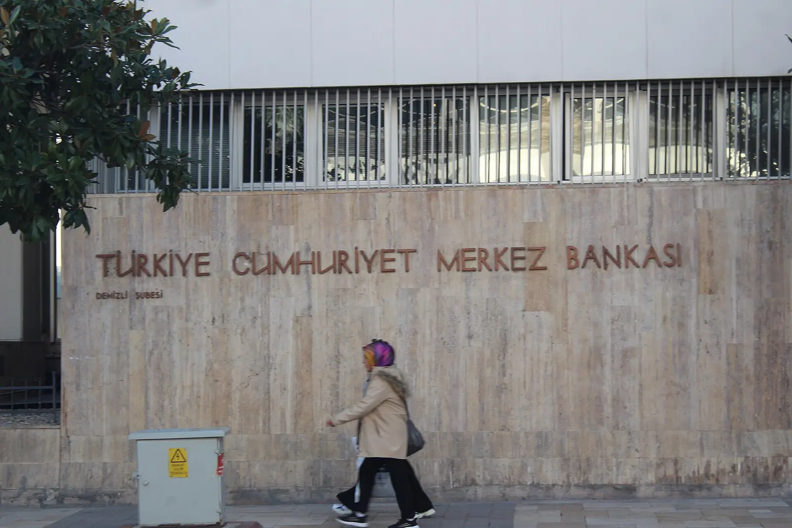 A pedestrian walks past the Turkiye Cumhuriyet Merkez Bankasi lettering carved into the travertine facade of a Central Bank of the Republic of Turkiye branch