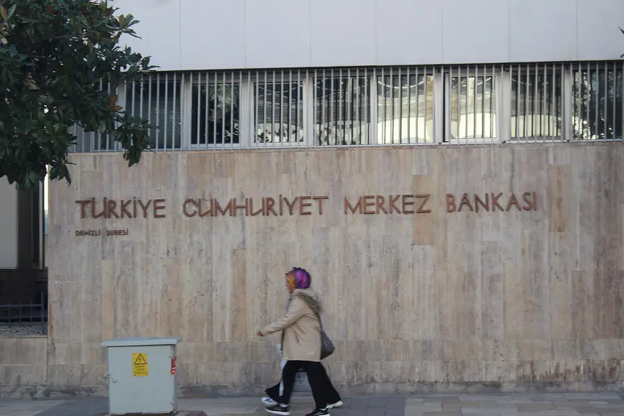 A pedestrian walks past the Turkiye Cumhuriyet Merkez Bankasi lettering carved into the travertine facade of a Central Bank of the Republic of Turkiye branch