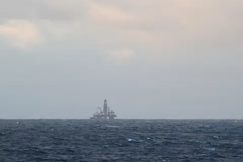 A semi-submersible oil and gas platform on a grey North Sea horizon off Scotland, photographed from the ship MV Pollux