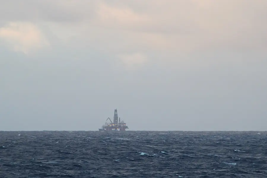A semi-submersible oil and gas platform on a grey North Sea horizon off Scotland, photographed from the ship MV Pollux