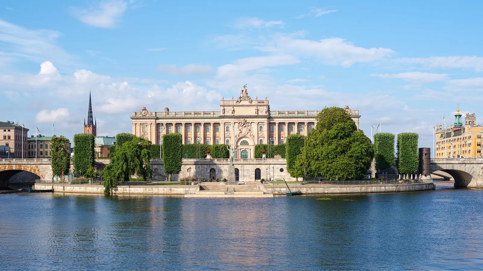 The Swedish Riksdag building on Helgeandsholmen in Stockholm seen across Norrstrom, with the national flag flying above the pediment