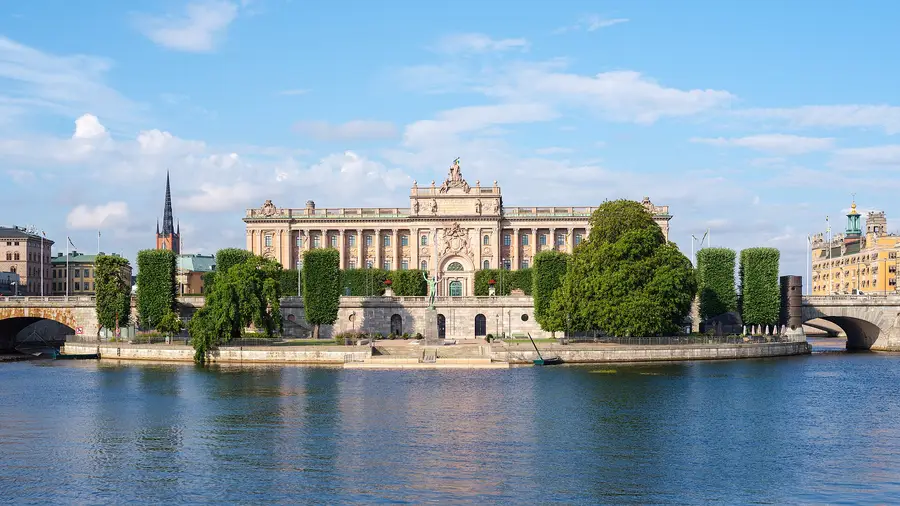 The Swedish Riksdag building on Helgeandsholmen in Stockholm seen across Norrstrom, with the national flag flying above the pediment