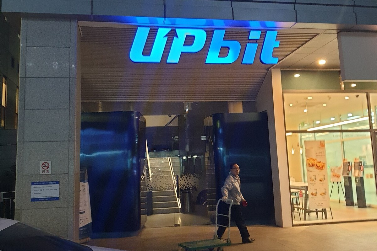 Entrance of the Upbit cryptocurrency exchange office in Seoul at night, lit blue Upbit sign above the door