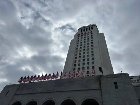 Los Angeles City Hall tower with a row of American flags along its roofline under a cloudy sky