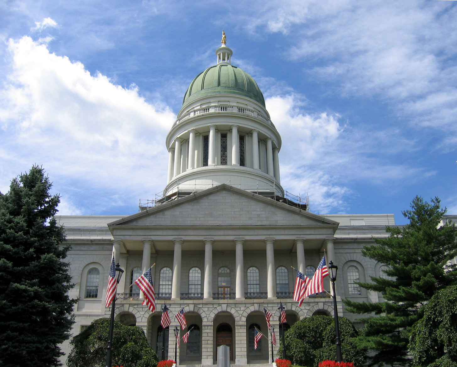 The Maine State House in Augusta, its green copper dome above a colonnaded portico hung with US flags