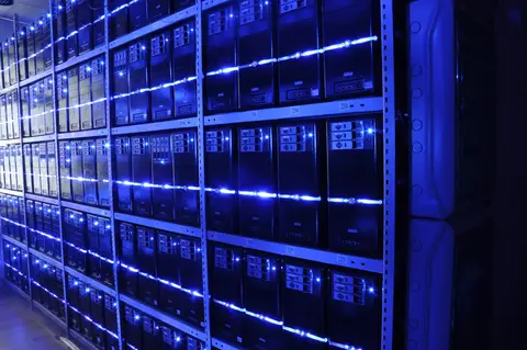 Rows of lit server towers on steel shelving inside a data centre, the kind of hardware that runs blockchain validator nodes