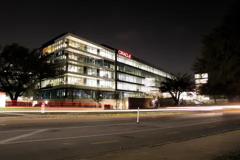Oracle office building on its Austin Texas riverside campus lit up at night with the red Oracle sign and car light trails