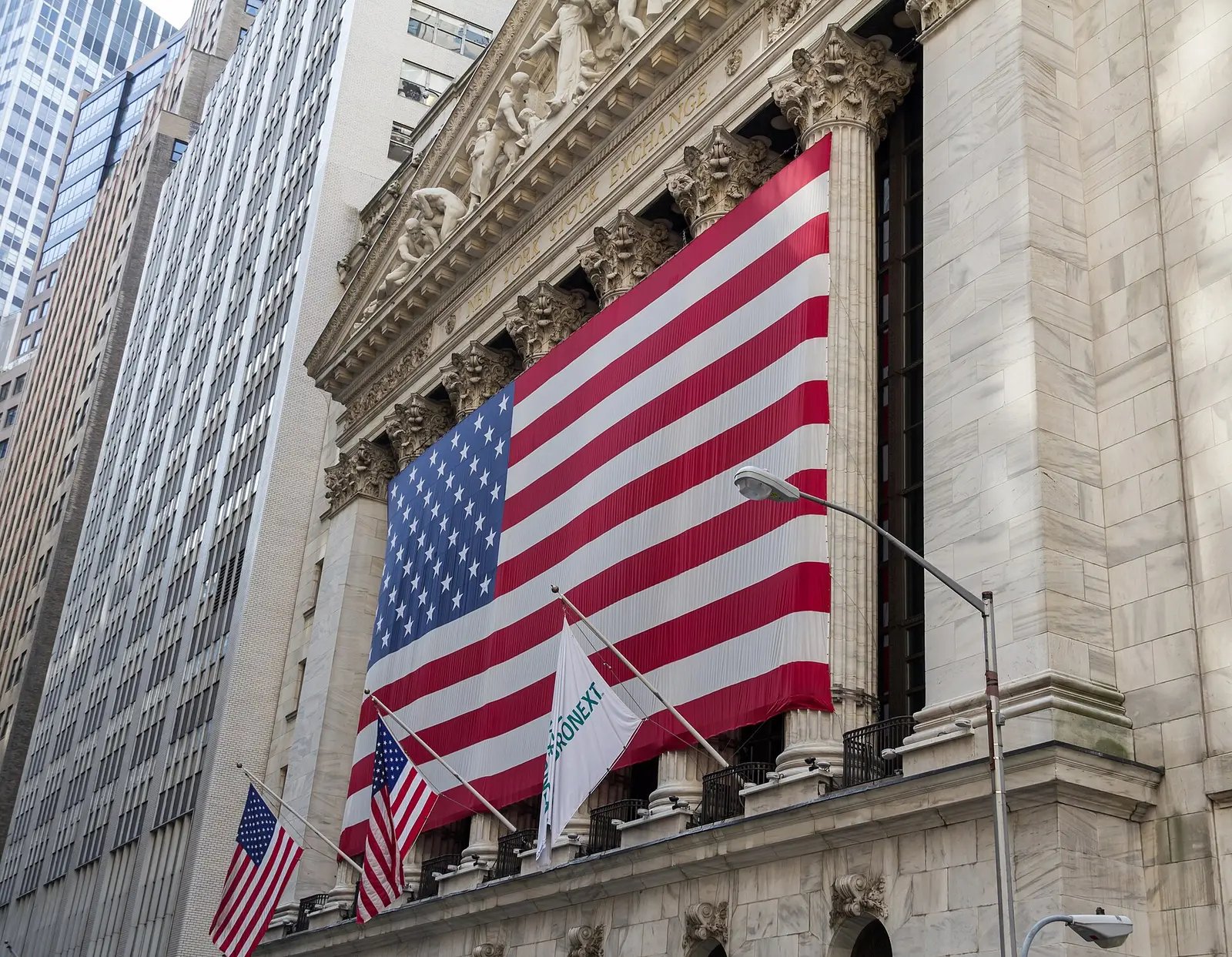 The New York Stock Exchange facade on Broad Street with a large United States flag hung across its Corinthian columns