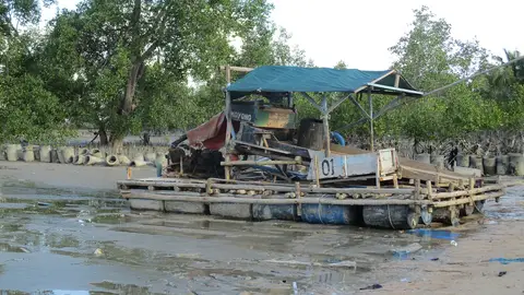 A floating tin mining pontoon moored on a tidal mudflat in Bangka Indonesia with a sluice box and pump mounted on a timber raft over oil drums